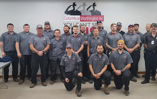 Group photo of Columbus Worthington Air HVAC technicians in gray uniforms, posing indoors in front of a company sign.